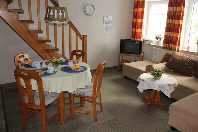 Wohn- und Essbereich der Ferienwohnung Carolinensiel-Harlesiel mit gedecktem Tisch, Sitzecke und Treppe nach oben