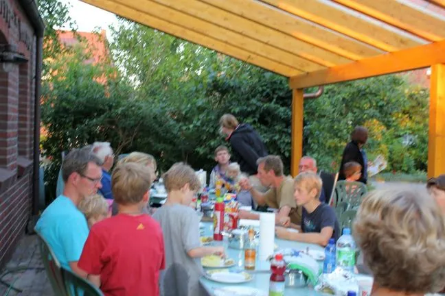 Gäste sitzen gemeinsam am langen Tisch unter dem Terrassendach