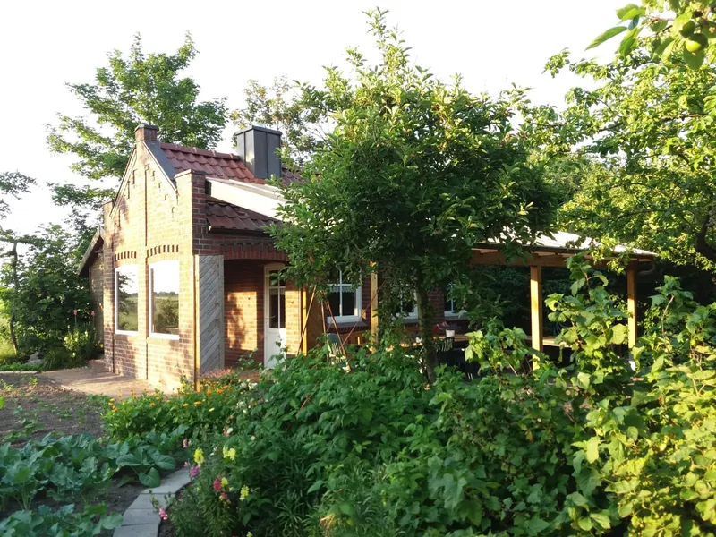 Das Gemeinschaftshaus aus Klinker mit Veranda, umgeben von Bäumen und Beeten