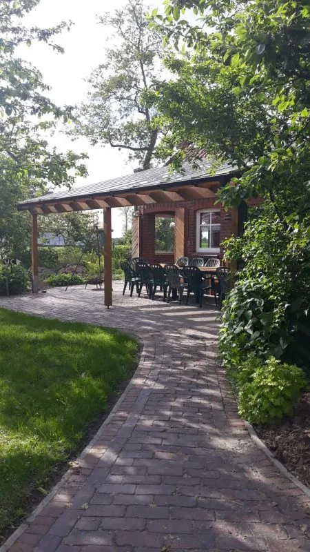 Gepflasterter Weg zur Pergola am Gemeinschaftshaus mit Tisch und Stühlen