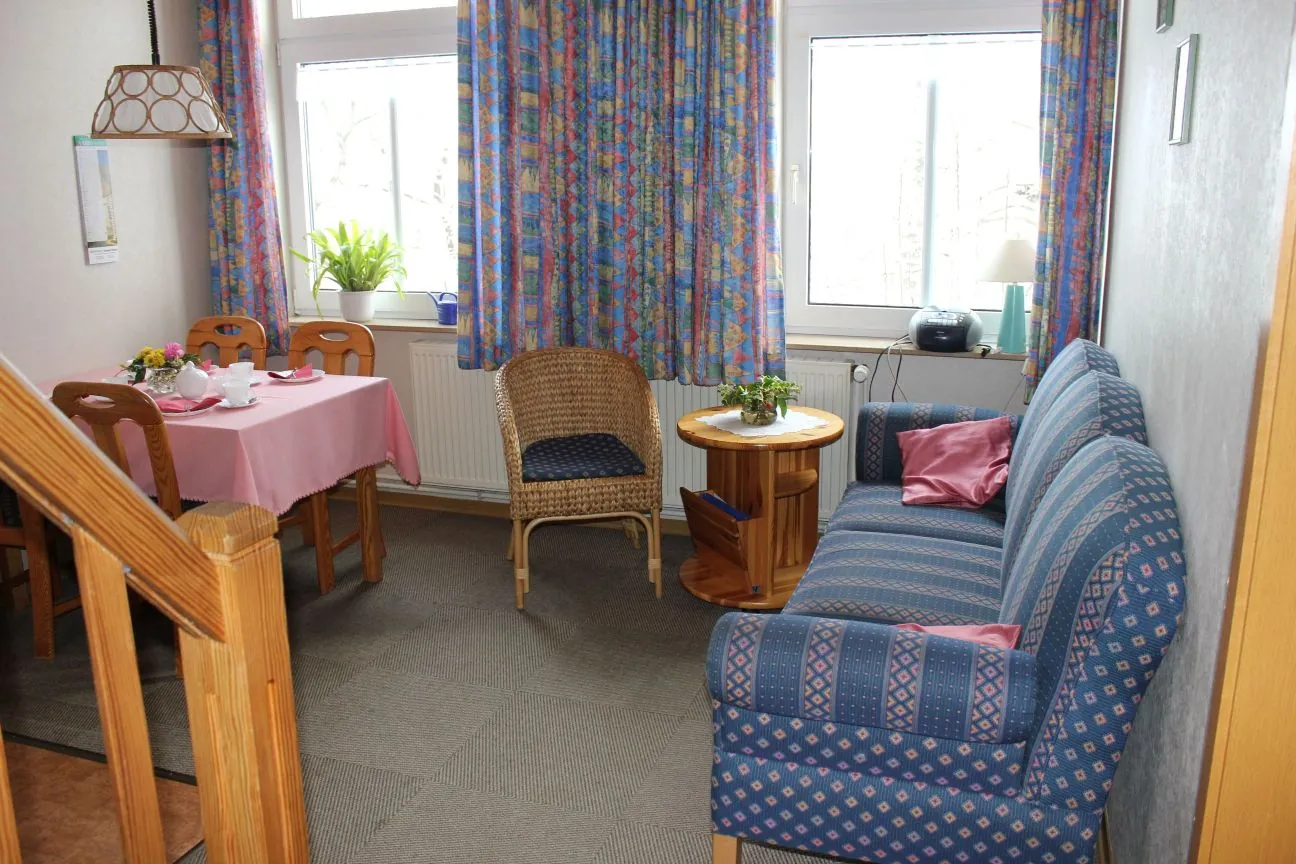 Wohn- und Essbereich der Ferienwohnung Wangerooge mit Sofa, Korbsessel und gedecktem Tisch